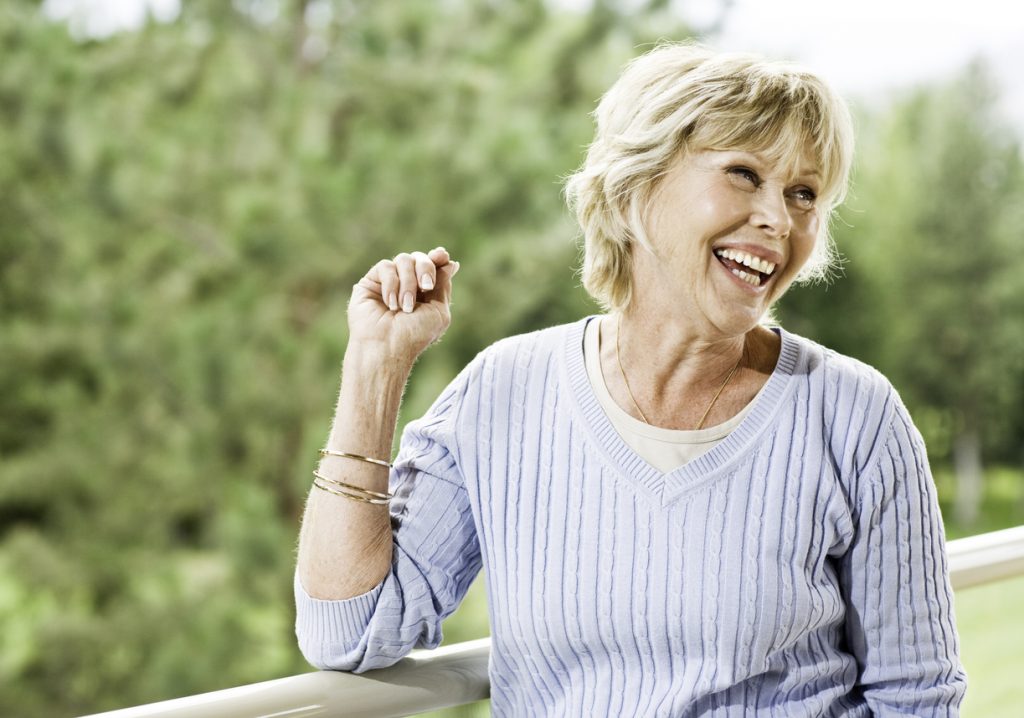 A candid, natural shot of a mature woman standing on her patio, laughing.